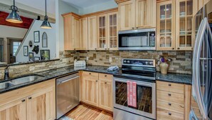 A modern kitchen with wooden cabinets, a stainless steel refrigerator, a microwave, and a dishwasher. - Adventure Hideaway at Eagles Nest (Banner Elk)