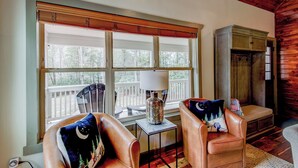 A cozy room with a large window, two leather armchairs with decorative pillows, a small table with a lamp, and a wooden cabinet. - Adventure Hideaway at Eagles Nest (Banner Elk)