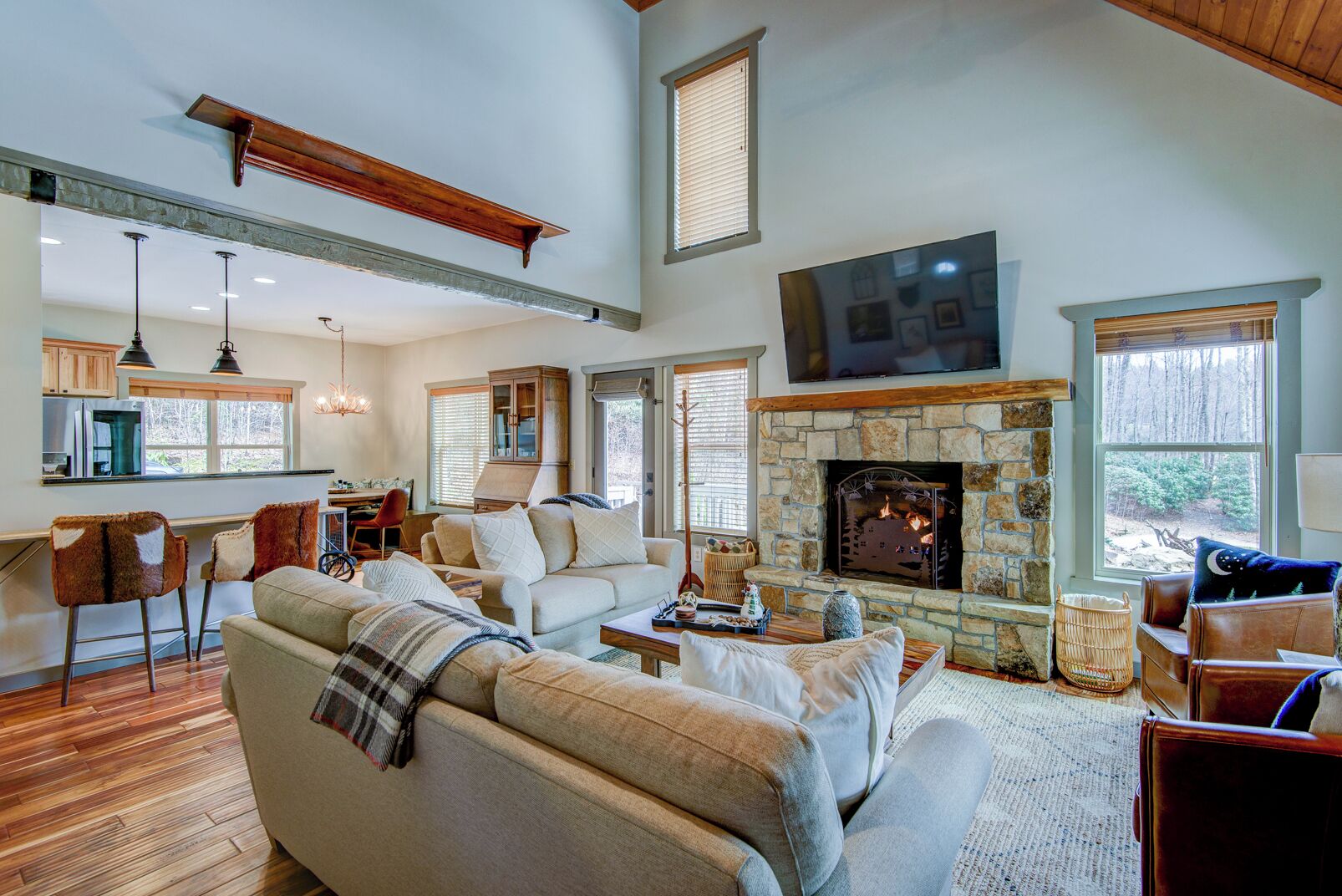 A spacious living room with a stone fireplace, a dining area, and a kitchen with wooden cabinets.