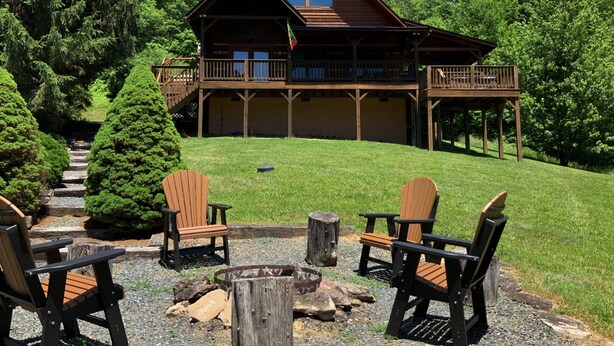 Eine Lodge mit einer Terrasse und einem Bereich mit Feuerstelle sowie Adirondack-Stühlen.