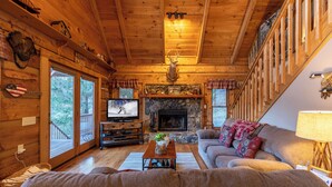 Ein gemütliches Cabin-Interieur mit Kamin aus Stein, Holzwänden, einem Fernseher und einer Couch.