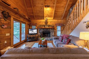 A cozy cabin interior with a stone fireplace, wooden walls, a television, and a couch. - Apple Cove (Vilas)