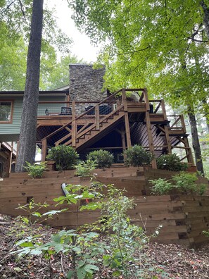 A multi-level wooden deck with a stone fireplace, surrounded by trees and plants. - Land Harbor Lodge (Newland)