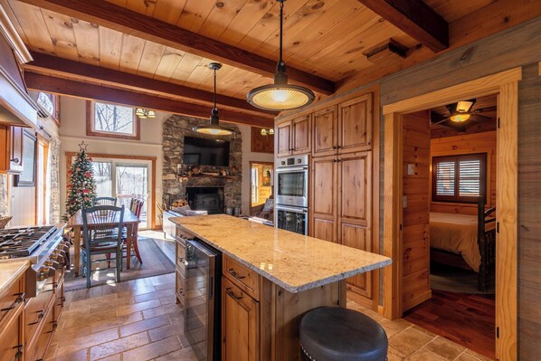 A spacious kitchen with wooden cabinets, a granite countertop, and a stone fireplace. - Land Harbor Lodge (Newland)