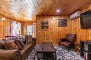 Interior acogedor de una cabaña con paredes de madera, un sofá de cuero, una mesa de centro, un sillón de cuero y una estantería.