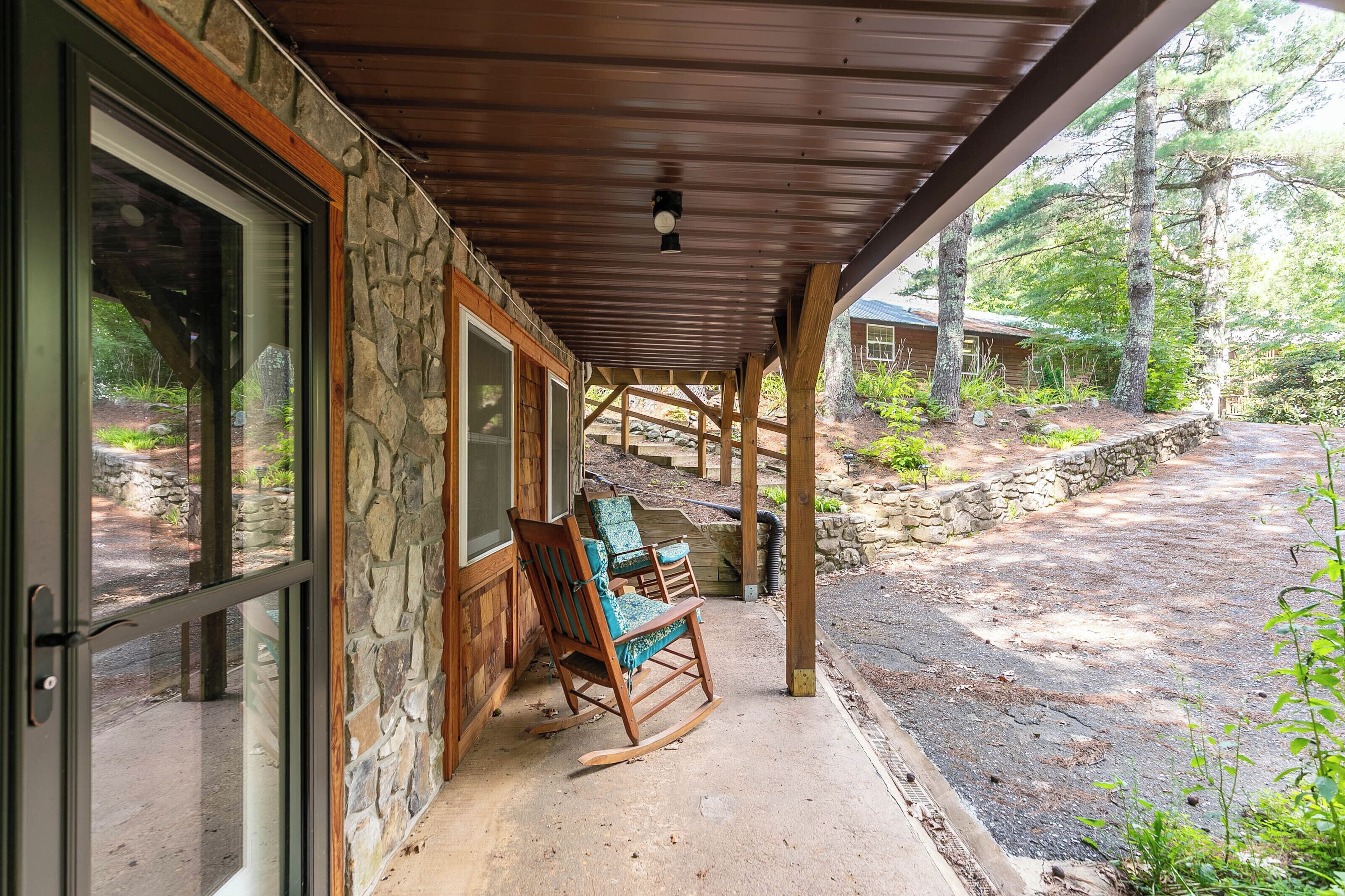 A covered porch with stone walls, wooden beams, and a view of a forested area.