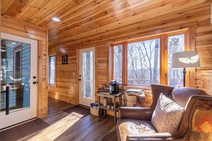 A cozy cabin interior with wooden walls, a leather sofa, a coffee station, and a view of trees through large windows. - Land Harbor Lodge (Newland)