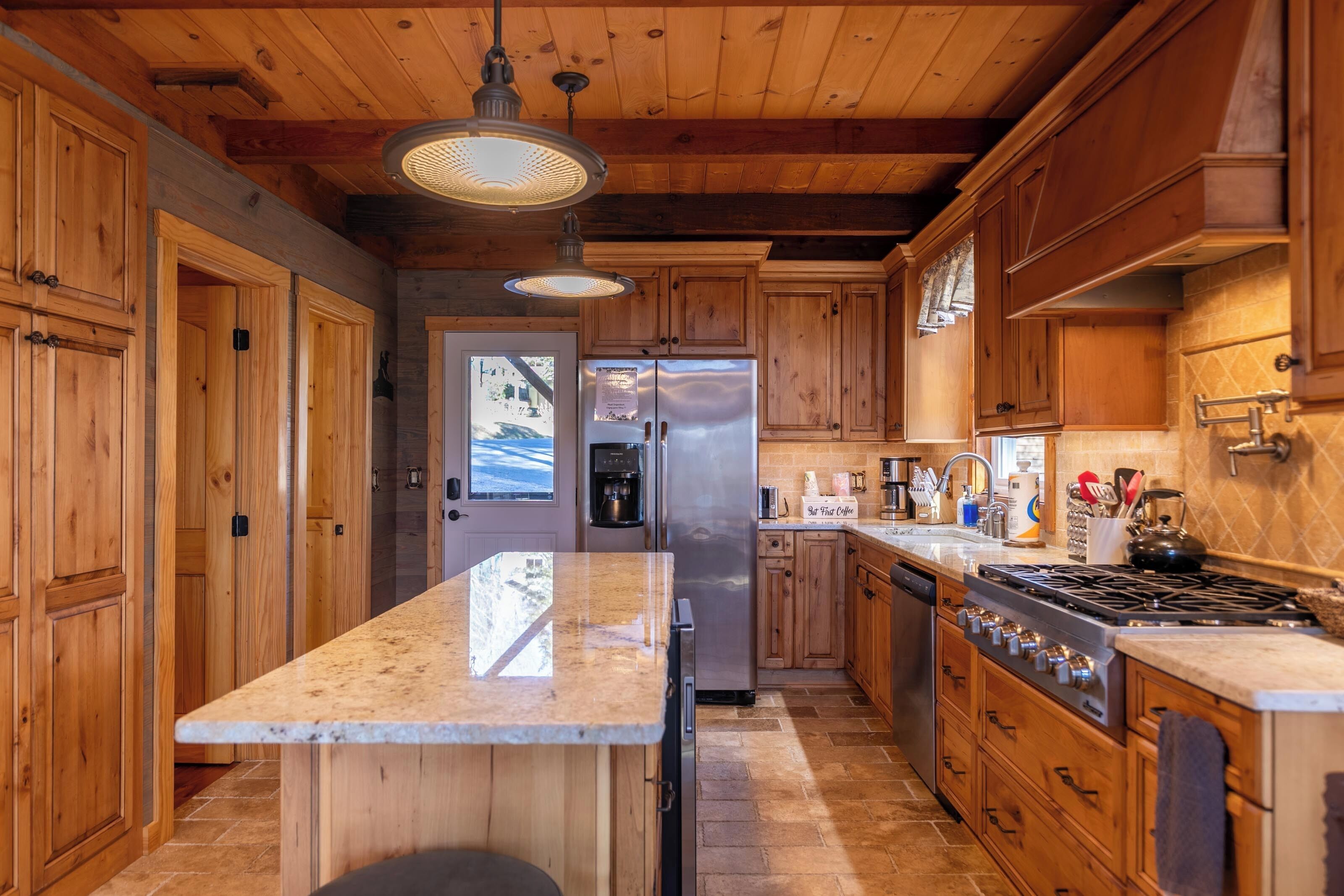 A kitchen with wooden cabinets, a stainless steel refrigerator, a built-in oven, and a large island with a marble countertop.