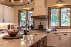 A modern kitchen with a large island, a stove, and a window with a view of trees. - Hidden Creek Cabin at Monteagle (Banner Elk)