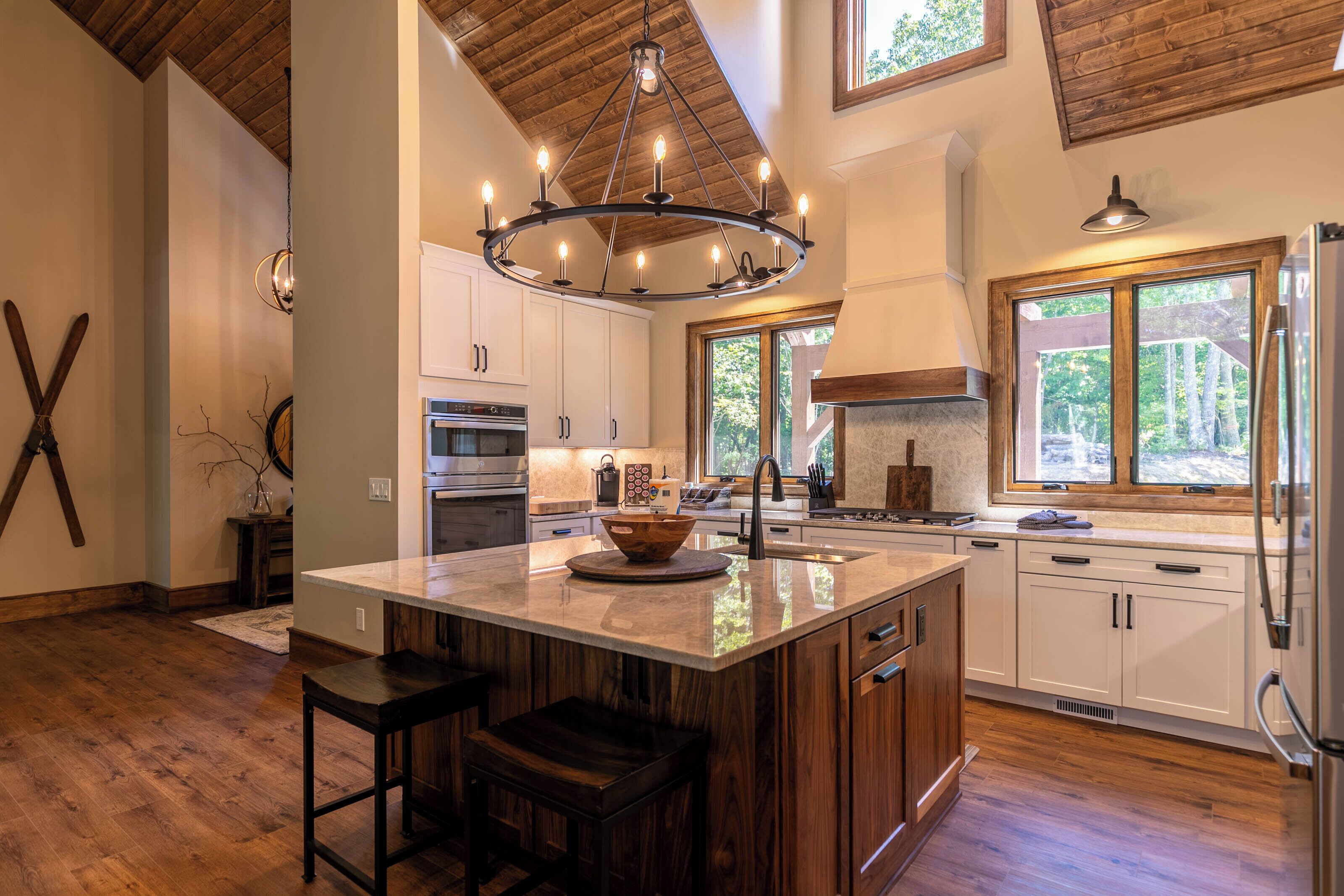 A kitchen with a large island, wooden cabinets, a chandelier, and a view of the outdoors.