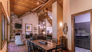 A spacious living area with a stone fireplace, wooden ceiling, and a dining table with chairs. - Hidden Creek Cabin at Monteagle (Banner Elk)