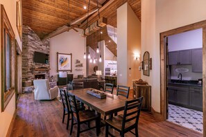 A spacious living area with a stone fireplace, wooden ceiling, and a dining table with chairs. - Hidden Creek Cabin at Monteagle (Banner Elk)