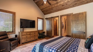 A bedroom with a large bed, wooden ceiling, a desk, and a television. - Hidden Creek Cabin at Monteagle (Banner Elk)