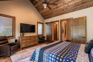 A bedroom with a large bed, wooden ceiling, a desk, and a television. - Hidden Creek Cabin at Monteagle (Banner Elk)