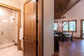A wooden door leading to a bathroom with a glass shower and a dining area with a table and chairs. - Hidden Creek Cabin at Monteagle (Banner Elk)