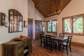 A dining area with a wooden table and chairs, a wooden ceiling, and large windows with a view of greenery. - Hidden Creek Cabin at Monteagle (Banner Elk)