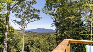A wooden deck overlooking a forested landscape with a mountain in the distance. - Hidden Creek Cabin at Monteagle (Banner Elk)