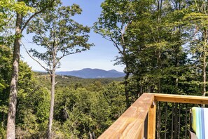 A wooden deck overlooking a forested landscape with a mountain in the distance. - Hidden Creek Cabin at Monteagle (Banner Elk)