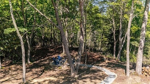 A forested area with a gravel path, trees, and blue Adirondack chairs. - Hidden Creek Cabin at Monteagle (Banner Elk)