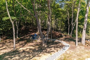 A forested area with a gravel path, trees, and blue Adirondack chairs. - Hidden Creek Cabin at Monteagle (Banner Elk)