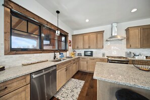 A modern kitchen with wooden cabinets, granite countertops, stainless steel appliances, and a large window. - Whispering Creek at Eagles Nest (Banner Elk)