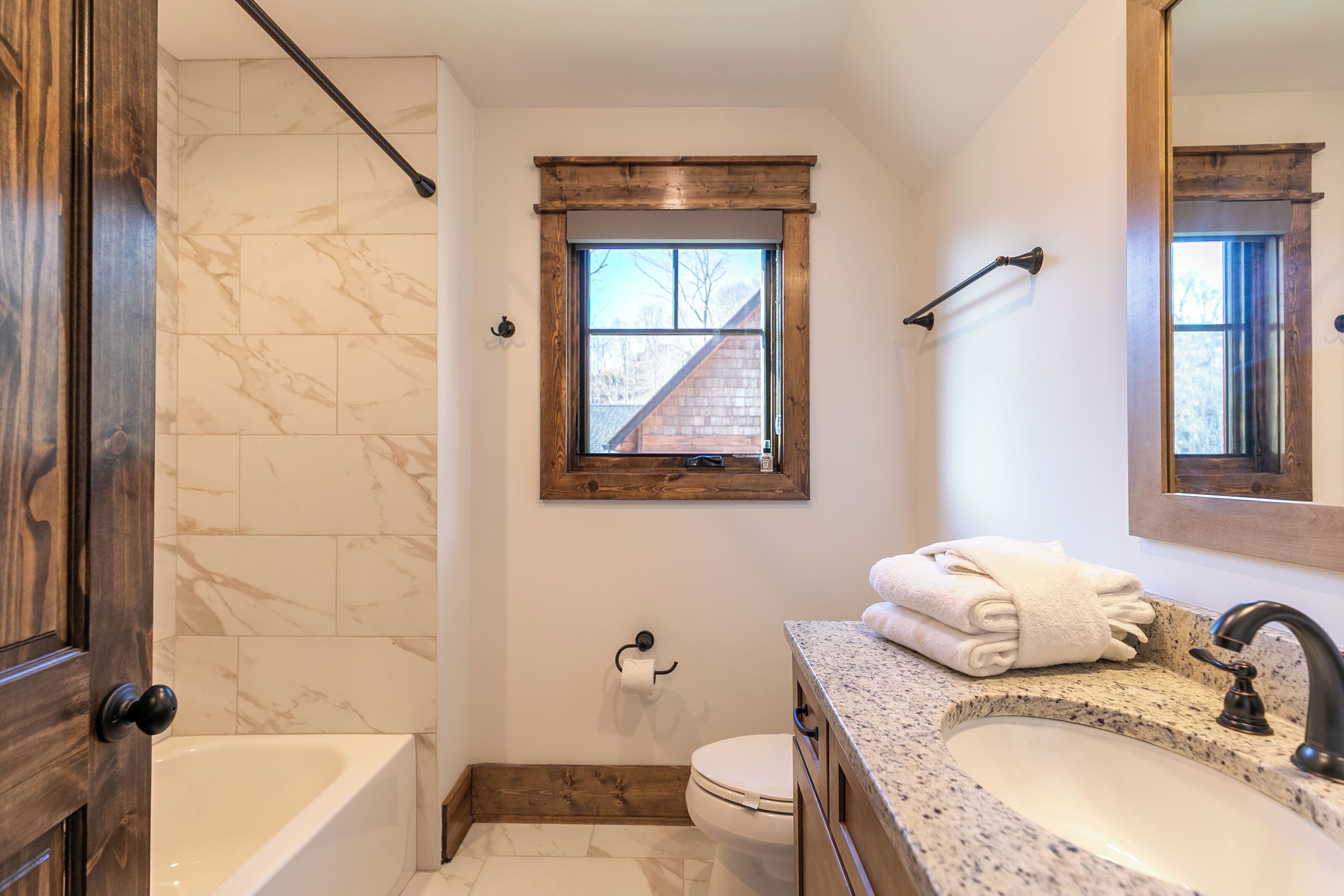 Een badkamer met bad, toilet, wastafel en een raam met uitzicht op een gebouw.