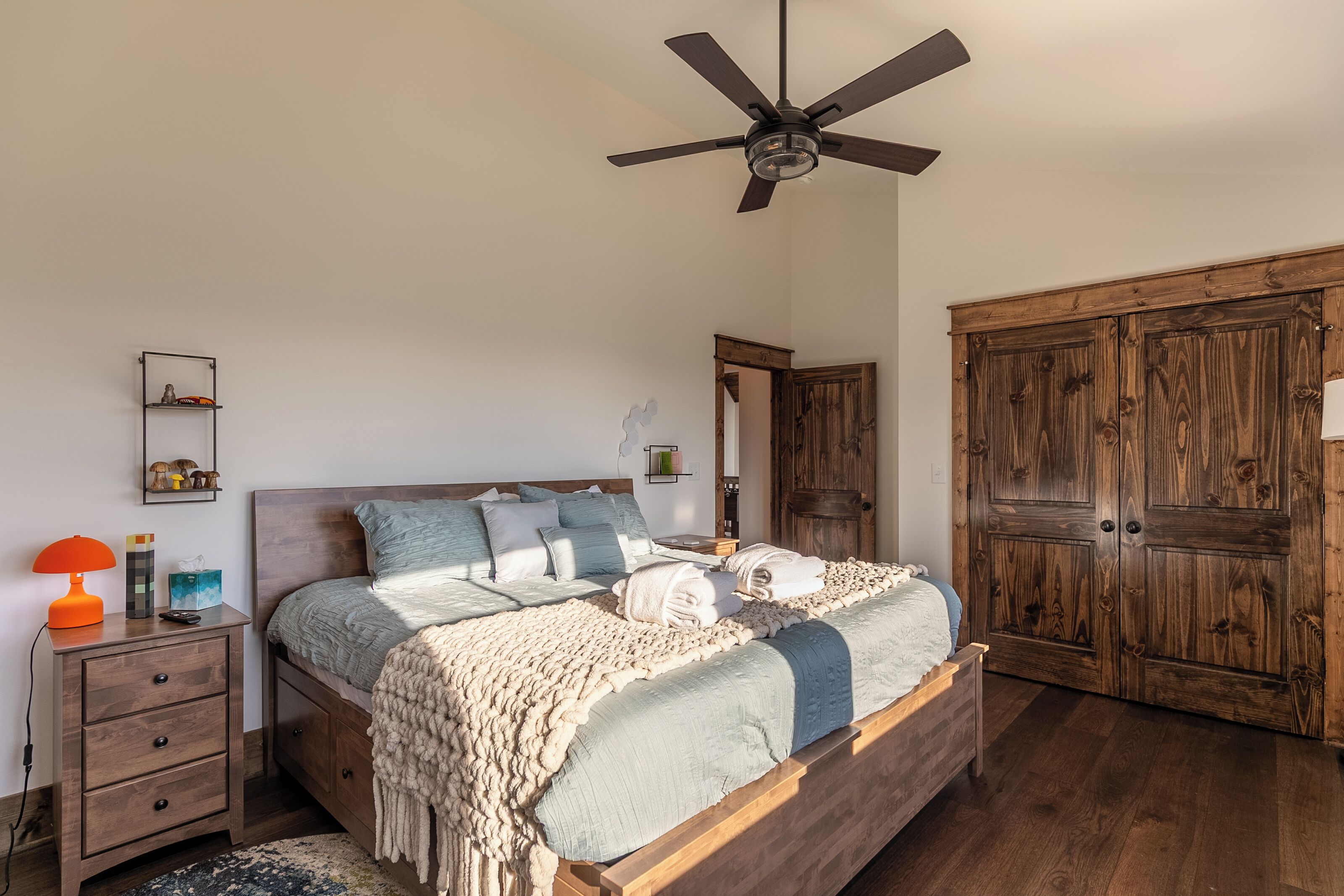 A bedroom with a bed, wooden wardrobe, nightstand, and a ceiling fan.