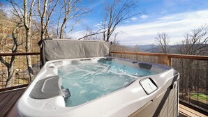 Ein Whirlpool auf einer Außenterrasse mit Blick auf Bäume und Hügel.