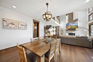 A spacious dining area with a wooden table and chairs, a chandelier, and a staircase leading to an upper level. - Whispering Creek at Eagles Nest (Banner Elk)