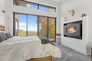 Ein modernes Schlafzimmer mit einem großen Bett, einem Kamin und einem weiten Ausblick durch raumhohe Fenster.