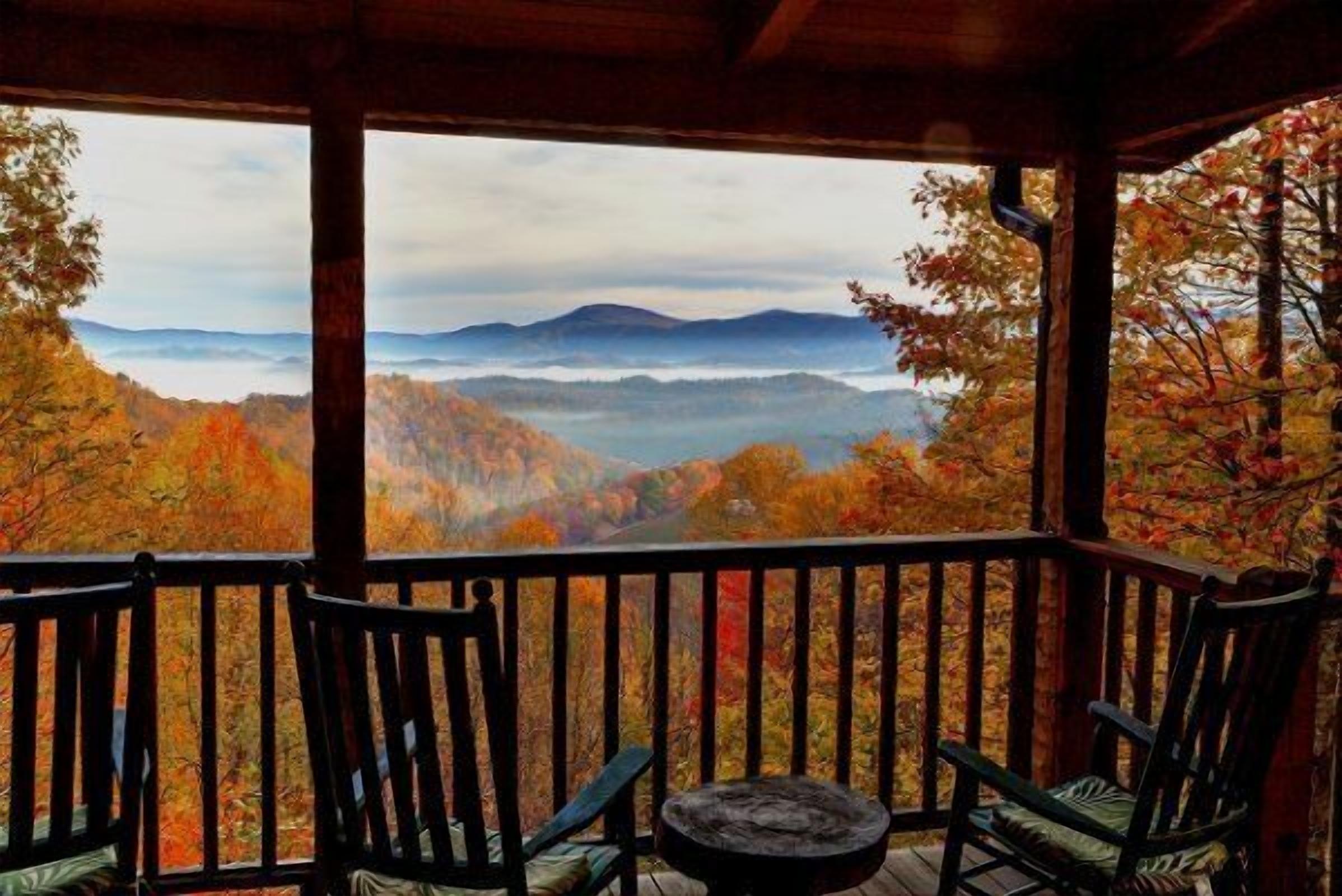 A porch with two chairs and a small table, overlooking a mountainous landscape with autumn foliage.