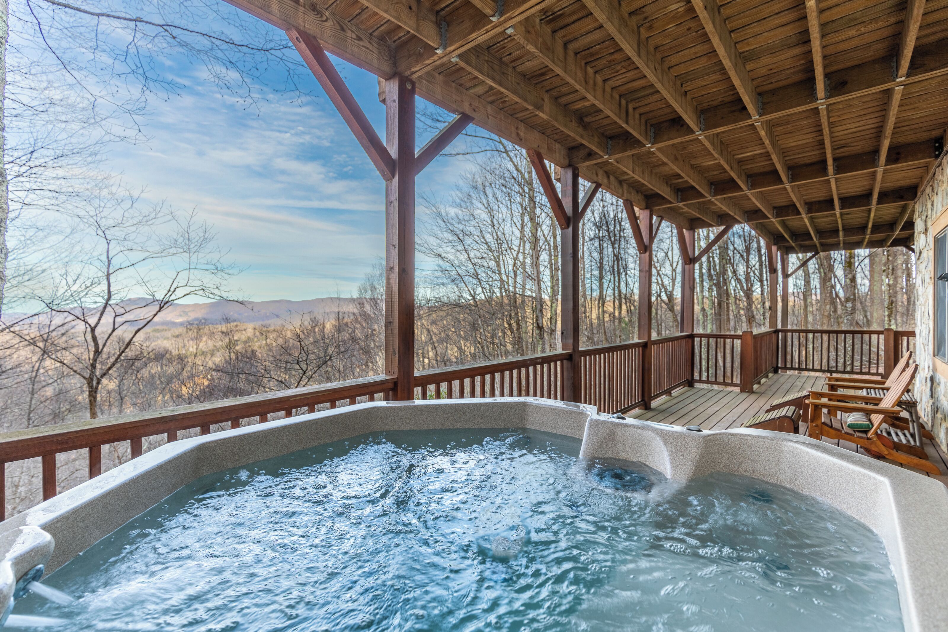A hot tub under a wooden deck with a view of mountains.