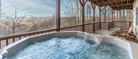 A hot tub under a wooden deck with a view of mountains.