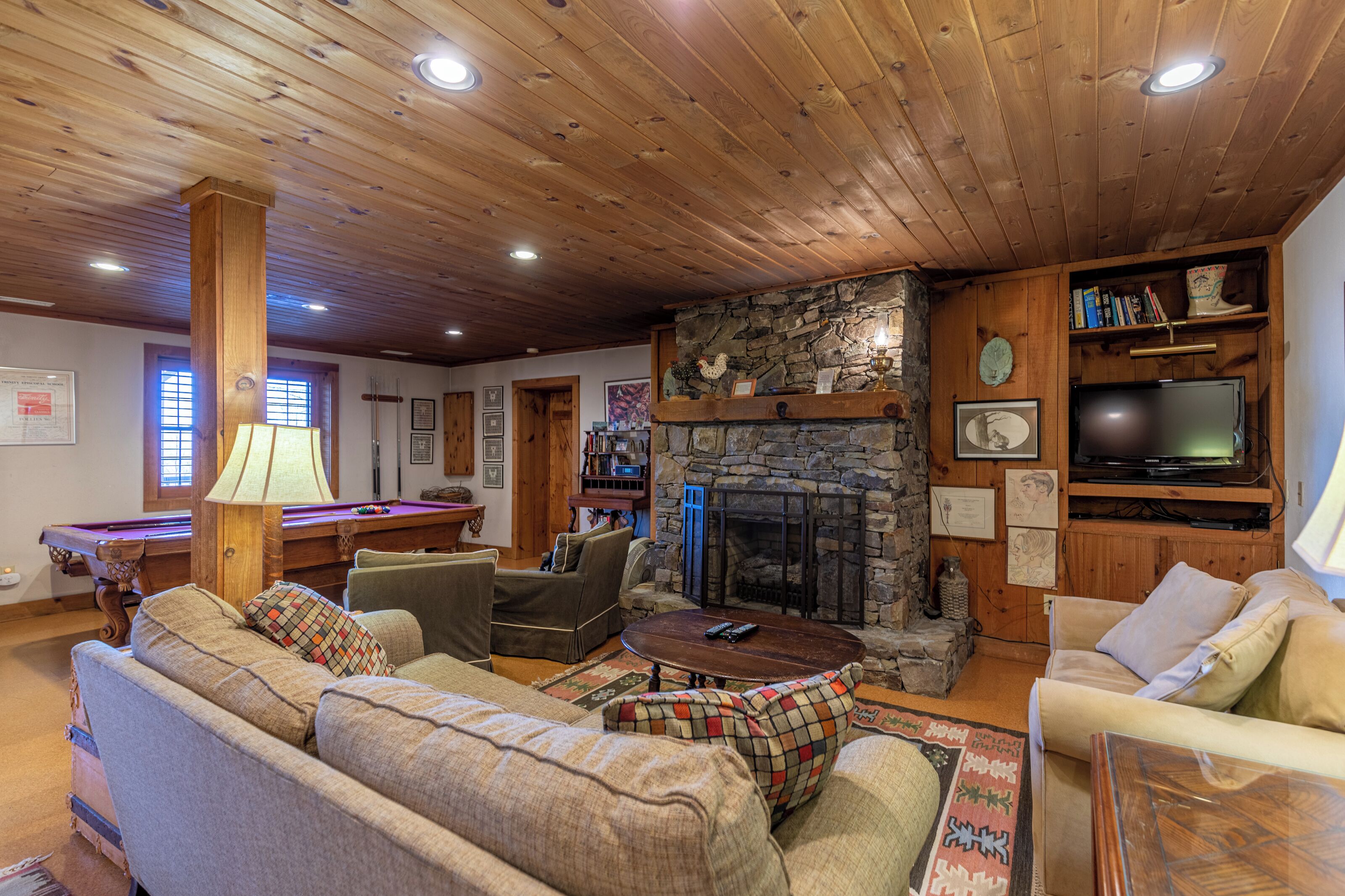 A cozy living room with a stone fireplace, wooden ceiling, and comfortable seating.