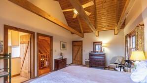 A bedroom with a large bed, wooden ceiling beams, a dresser, a chair, and a door leading to another room. - Journeys End at Valle Crucis (Banner Elk)