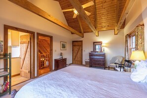 A bedroom with a large bed, wooden ceiling beams, a dresser, a chair, and a door leading to another room. - Journeys End at Valle Crucis (Banner Elk)