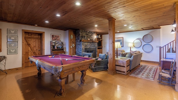 A pool table in a room with wooden ceilings and walls, a stone fireplace, a sofa, and a staircase. - Journeys End at Valle Crucis (Banner Elk)