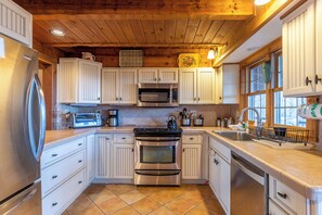 A kitchen with white cabinets, stainless steel appliances, and a wooden ceiling. - Journeys End at Valle Crucis (Banner Elk)