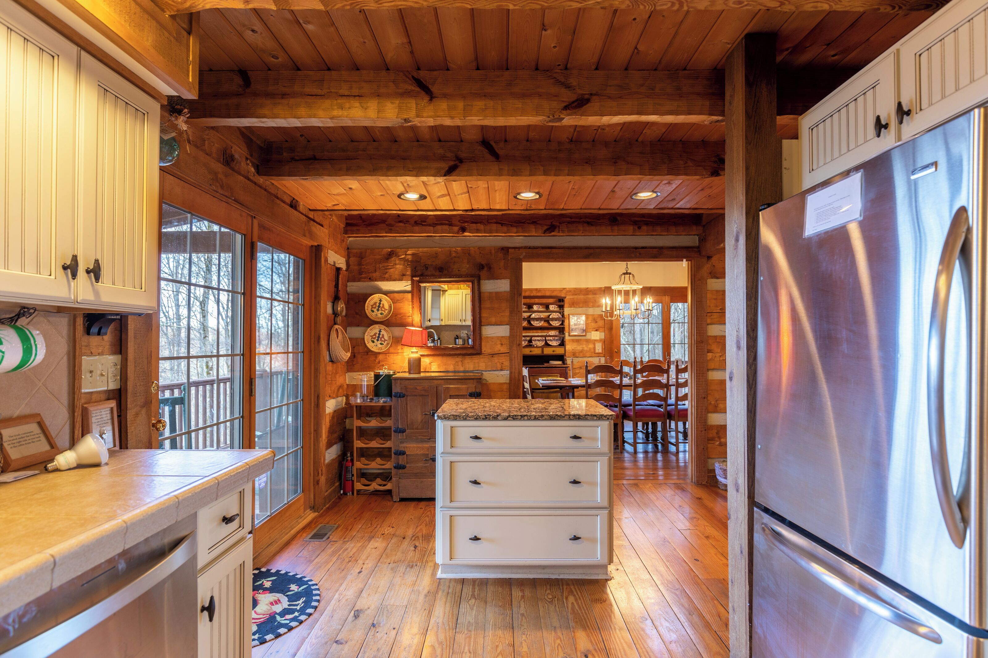 A kitchen with wooden beams, a stainless steel refrigerator, and a dining area with wooden chairs.