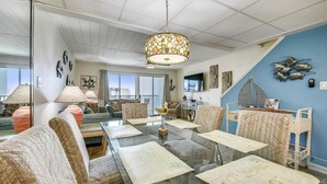 Un salón amplio con una gran mesa de vidrio, asientos cómodos, televisión y decoración en la pared.