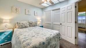 Un dormitorio con cama, mesitas de noche, ventilador de techo y puerta que da a un balcón.