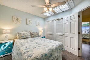 Ein Schlafzimmer mit einem Bett, Nachttischen, einem Deckenventilator und einer Tür, die auf einen Balkon führt.