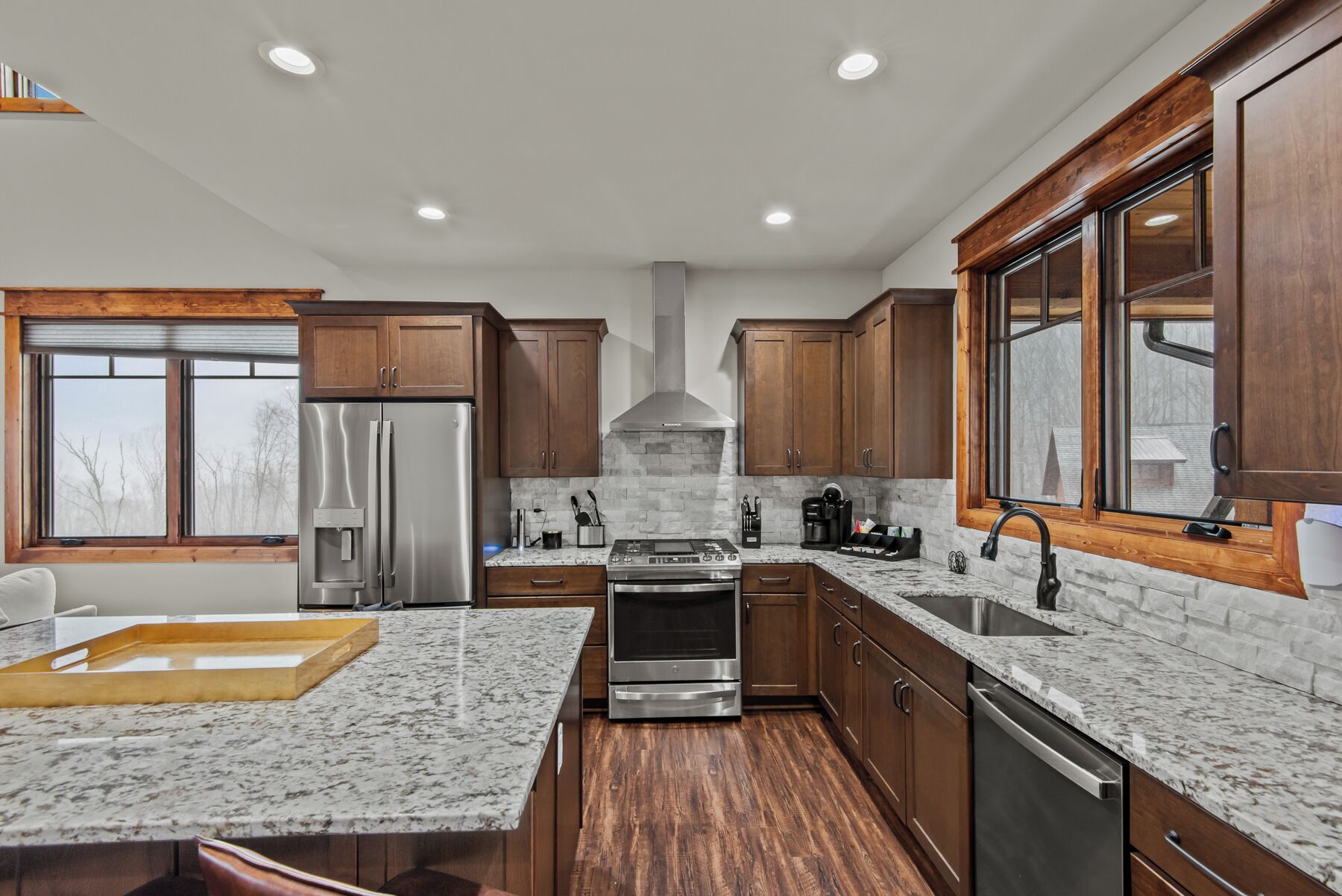 A modern kitchen with wooden cabinets, granite countertops, stainless steel appliances, and a large window.