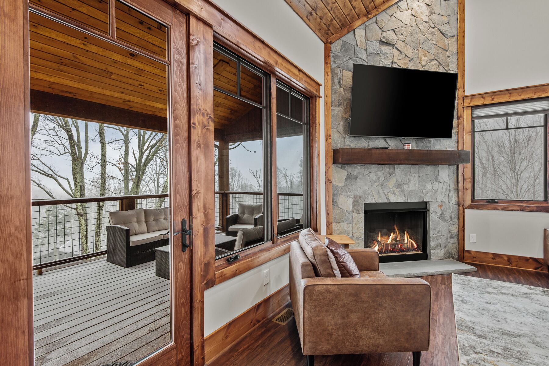 Un salon chaleureux avec une cheminée en pierre, des poutres en bois et de grandes fenêtres donnant sur un paysage enneigé.