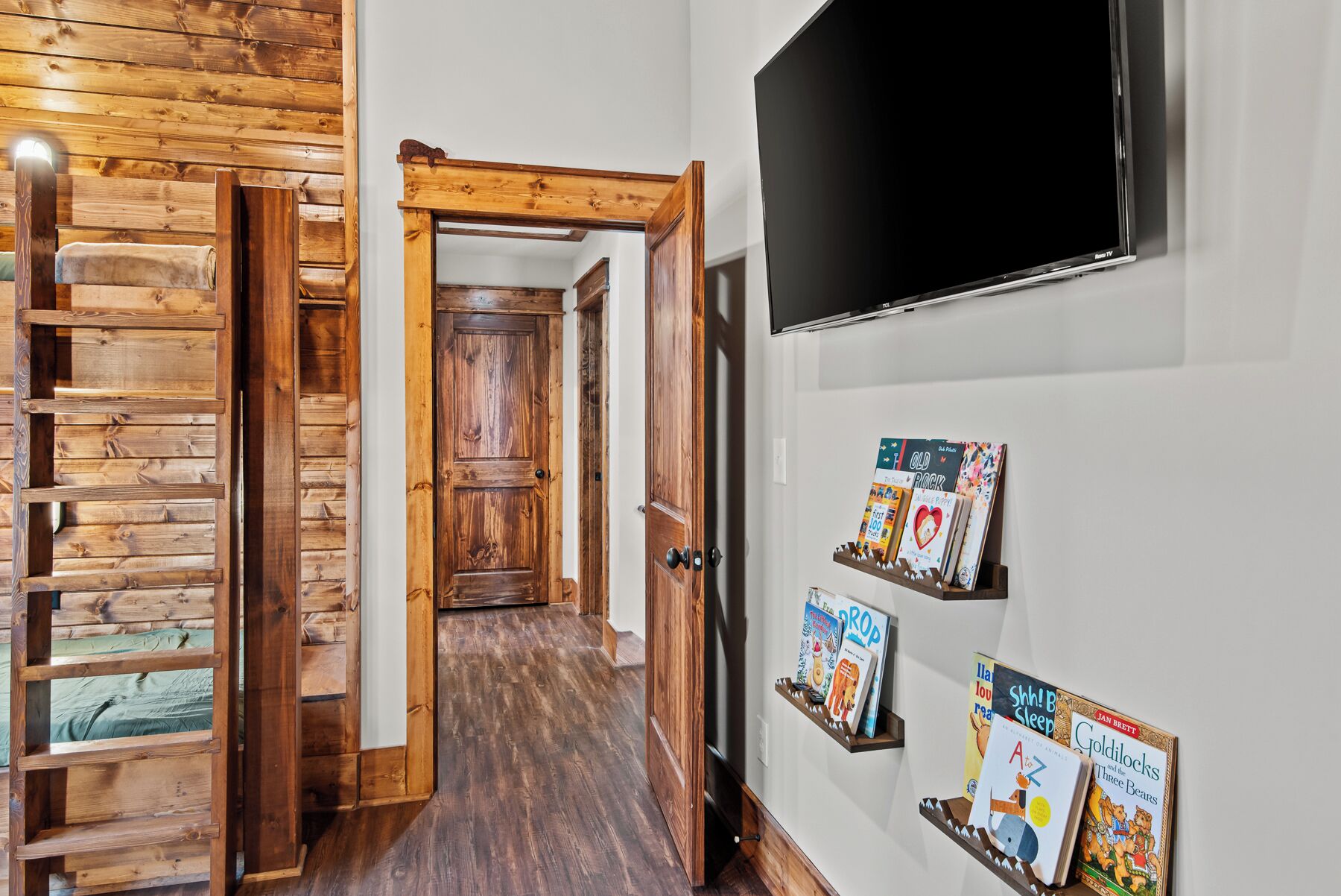 A wooden interior hallway with a TV mounted on the wall and bookshelves with children's books.