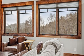 A room with a large window, a sofa, and a small wooden table. - Cornerstone Cabin at Eagles Nest (Banner Elk)