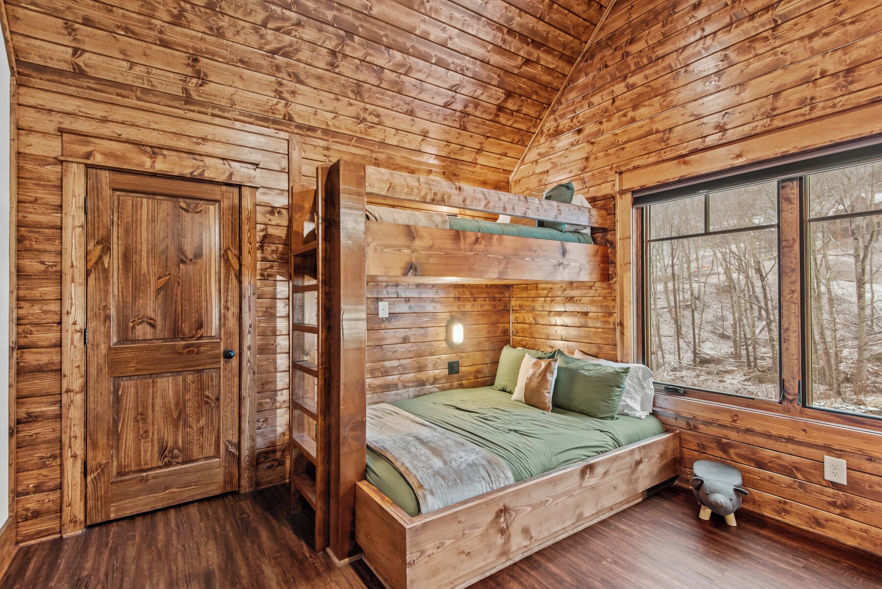 A wooden cabin interior with a bunk bed, a door, and a window.
