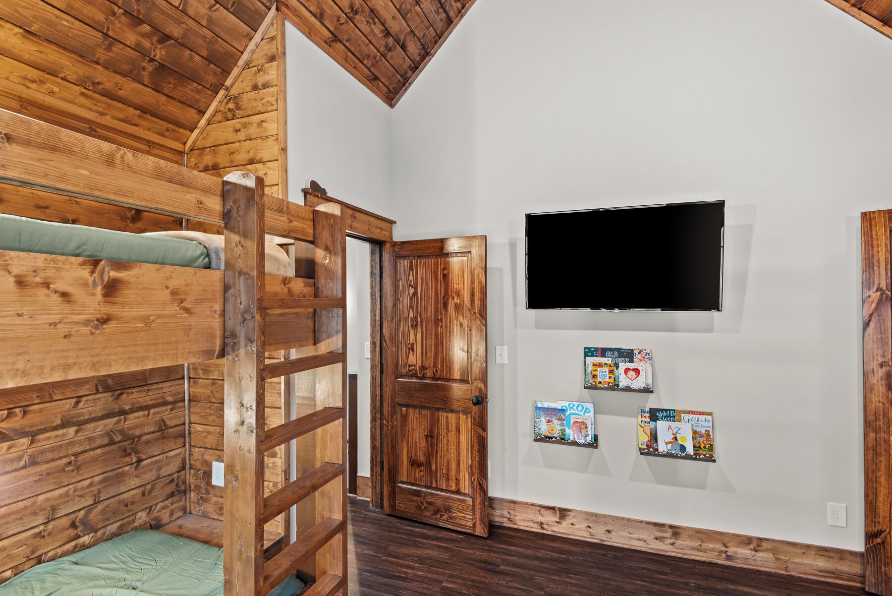 A room with a bunk bed, a wooden ladder, a television, and children's books on the wall.