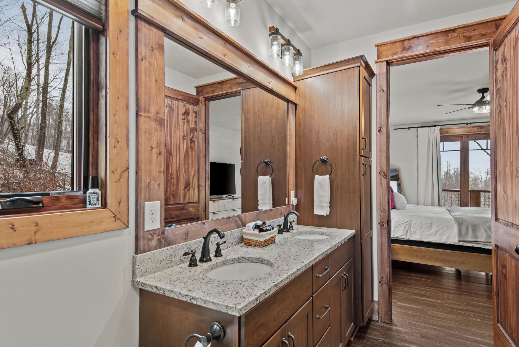 A bathroom with wooden cabinetry, a granite countertop, a double sink, and a large mirror.