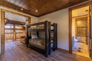 Ein Stockbett in einem Zimmer mit Holzböden und Holzbalkendecke. Ein Badezimmer mit Badewanne und Toilette ist durch eine offene Tür sichtbar.